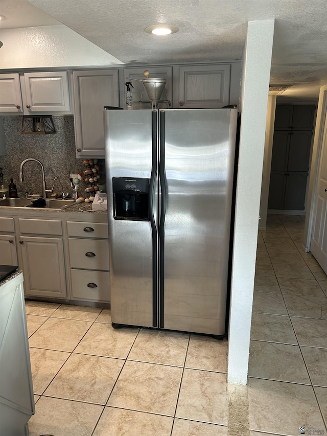 kitchen featuring light tile patterned floors, gray cabinetry, stainless steel fridge, and sink