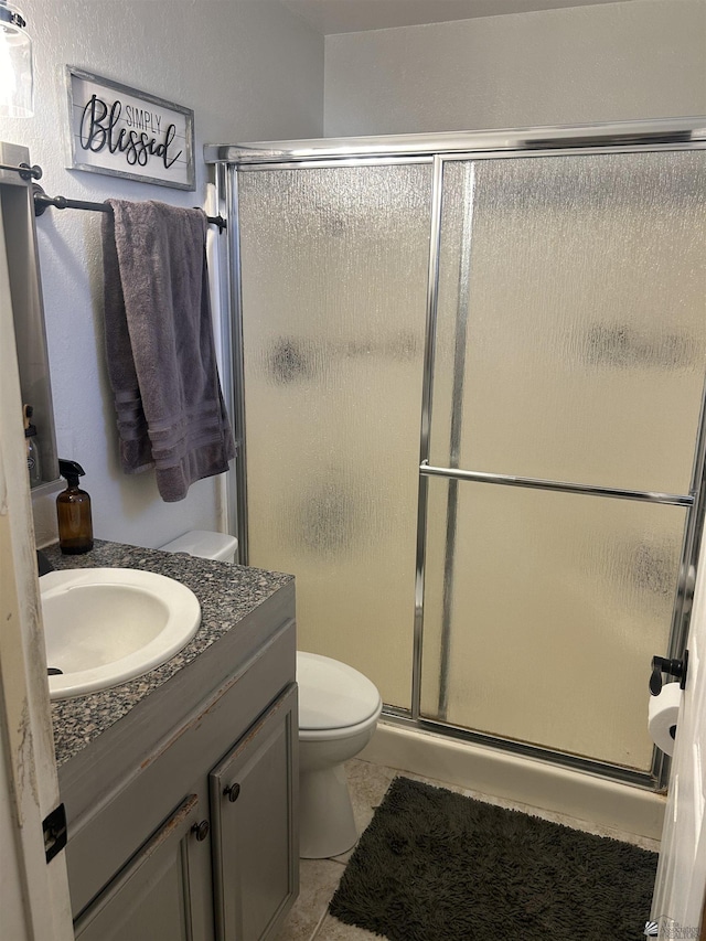 bathroom featuring tile patterned floors, a shower with door, toilet, and vanity