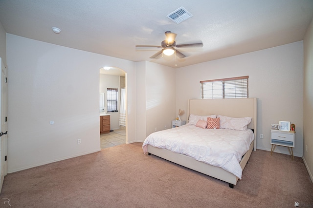 bedroom featuring light colored carpet, ensuite bath, and ceiling fan