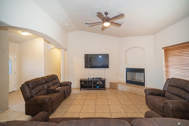 living room with decorative columns, vaulted ceiling, ceiling fan, a tile fireplace, and light tile patterned floors