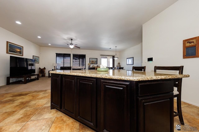 kitchen featuring decorative light fixtures, a kitchen breakfast bar, ceiling fan, light stone countertops, and a kitchen island with sink