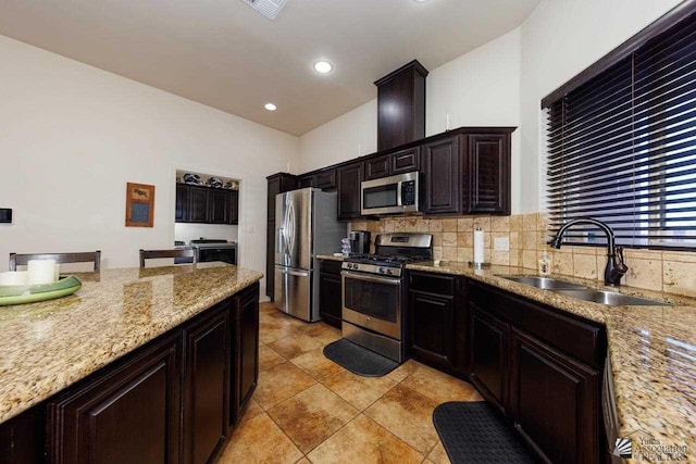 kitchen featuring appliances with stainless steel finishes, sink, decorative backsplash, light stone countertops, and dark brown cabinets