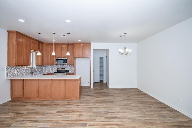 kitchen featuring pendant lighting, an inviting chandelier, appliances with stainless steel finishes, light hardwood / wood-style floors, and kitchen peninsula