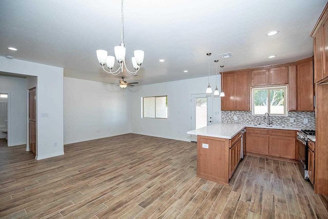 kitchen with kitchen peninsula, gas stove, ceiling fan with notable chandelier, sink, and decorative light fixtures