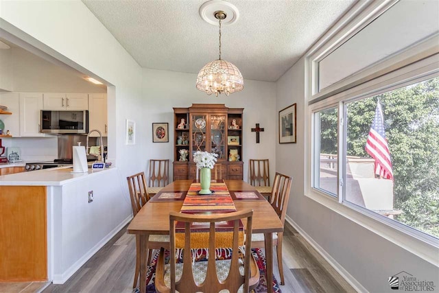 dining room with a healthy amount of sunlight, an inviting chandelier, a textured ceiling, and dark hardwood / wood-style flooring