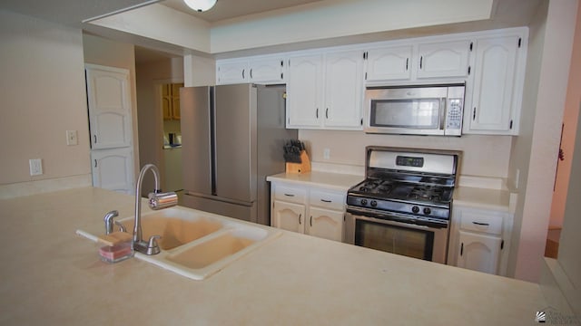 kitchen with a sink, stainless steel appliances, light countertops, and white cabinets