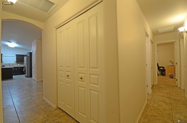 hallway with visible vents, arched walkways, lofted ceiling, and light tile patterned flooring