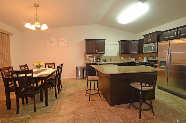 kitchen with a center island, appliances with stainless steel finishes, a breakfast bar area, decorative backsplash, and vaulted ceiling