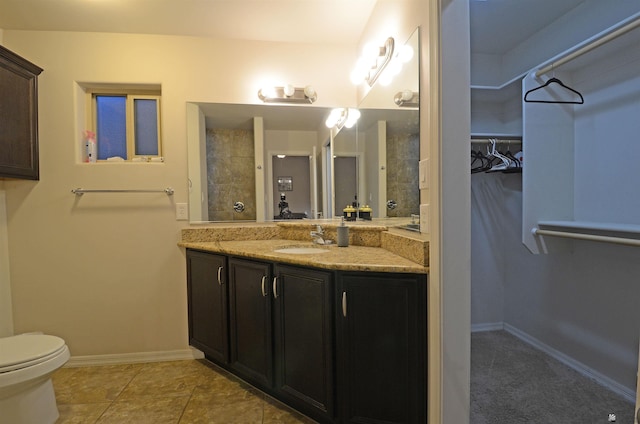 full bath with a walk in closet, toilet, tile patterned flooring, baseboards, and vanity