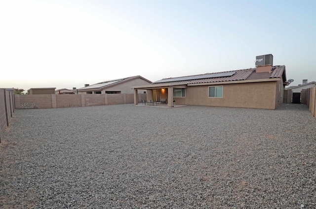 rear view of property with a tiled roof, roof mounted solar panels, stucco siding, central AC unit, and a fenced backyard