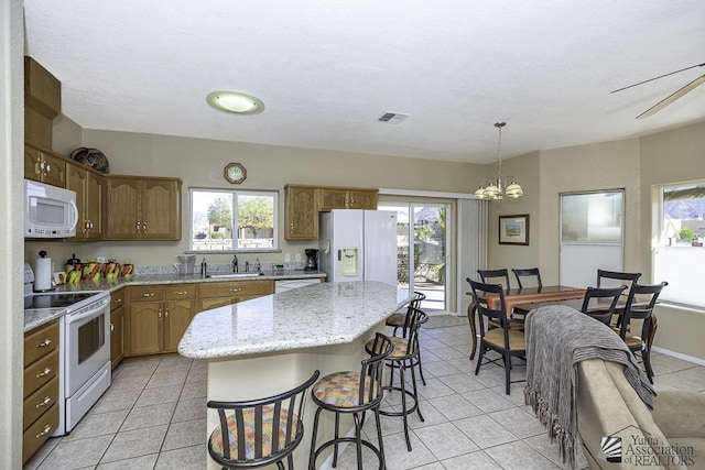 kitchen with white appliances, sink, light tile patterned floors, a kitchen island, and hanging light fixtures