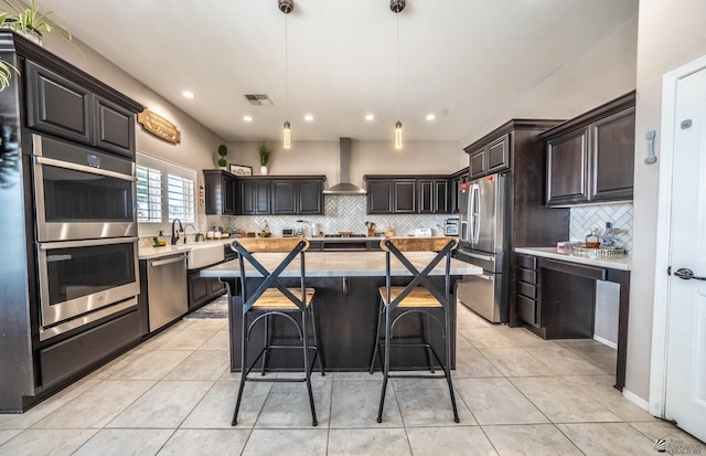 kitchen with wall chimney exhaust hood, a center island, dark brown cabinets, pendant lighting, and stainless steel appliances