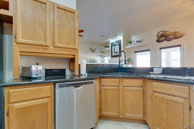 kitchen with dark stone counters, stainless steel dishwasher, light tile patterned flooring, and a sink