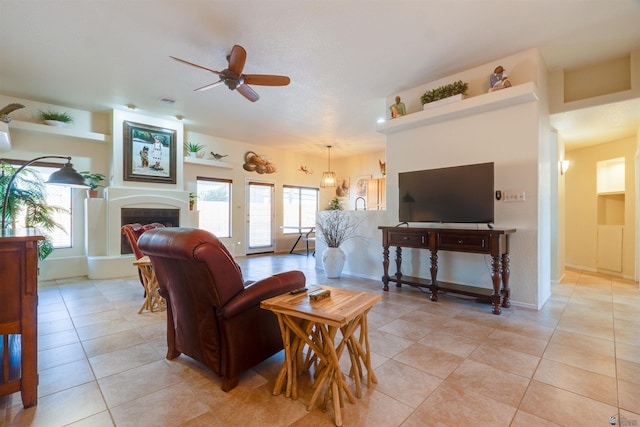 living area with ceiling fan, light tile patterned flooring, a tile fireplace, and baseboards