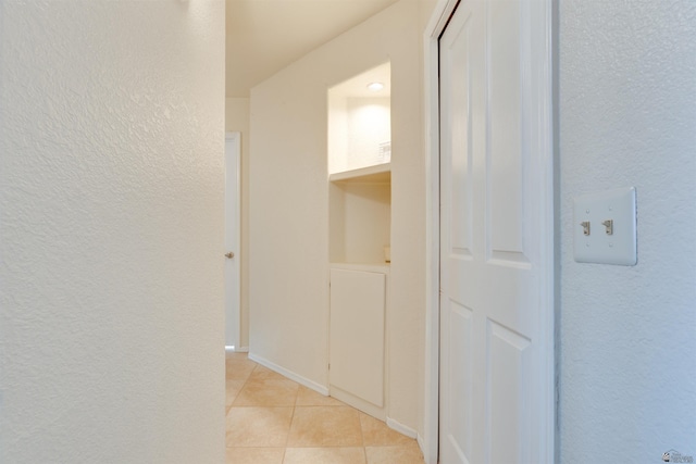 hall with light tile patterned flooring, a textured wall, and baseboards