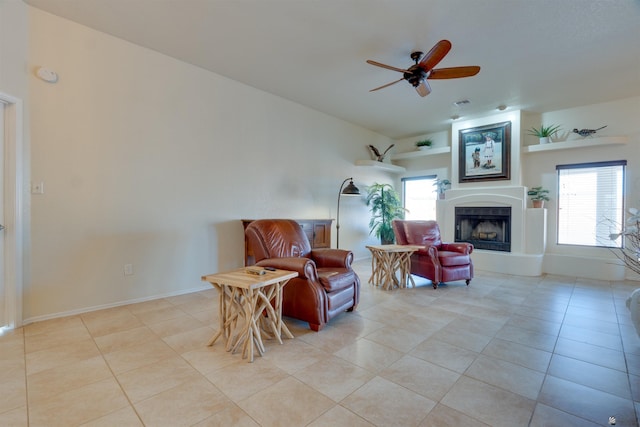 living area with a fireplace with raised hearth, ceiling fan, plenty of natural light, and light tile patterned flooring