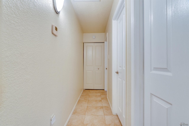 hallway featuring light tile patterned floors, baseboards, and a textured wall