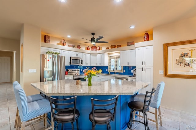 kitchen featuring sink, appliances with stainless steel finishes, light stone countertops, white cabinets, and a kitchen bar