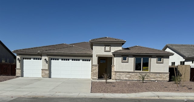 prairie-style home with stone siding, fence, an attached garage, and concrete driveway