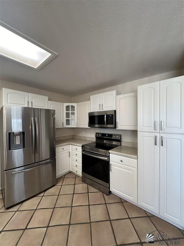 kitchen featuring light tile patterned flooring, white cabinets, stainless steel appliances, and a textured ceiling