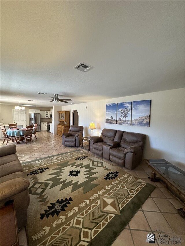 tiled living room with ceiling fan with notable chandelier