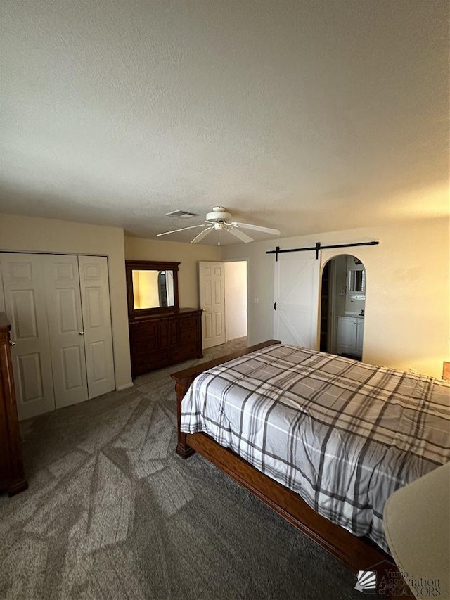 carpeted bedroom featuring ceiling fan, a barn door, a textured ceiling, and a closet