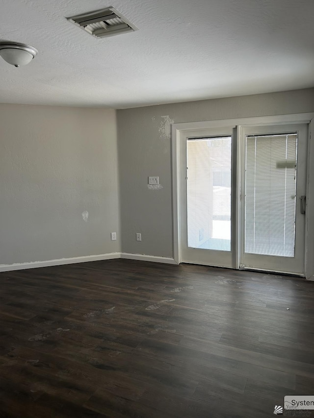 unfurnished room featuring visible vents, a textured ceiling, dark wood-type flooring, and baseboards