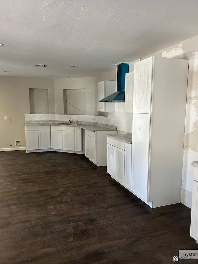 kitchen with visible vents, a sink, wall chimney exhaust hood, decorative backsplash, and dark wood-style flooring