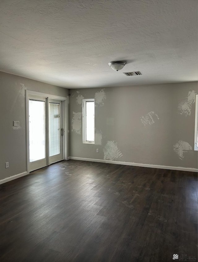 spare room featuring baseboards, visible vents, dark wood-style flooring, and a textured ceiling