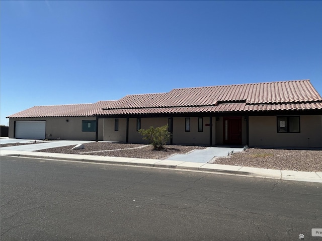 ranch-style house with a tiled roof, an attached garage, and stucco siding