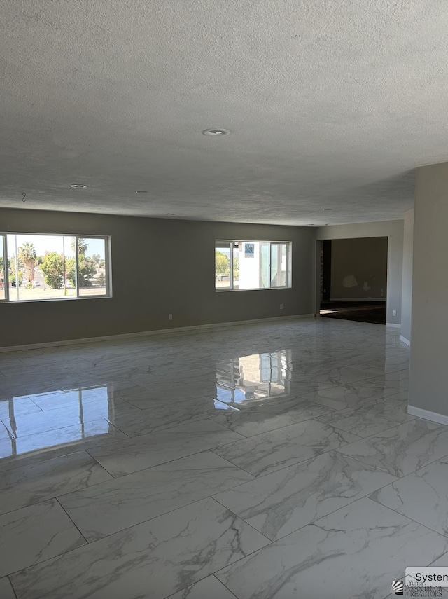 spare room featuring baseboards, marble finish floor, and a textured ceiling