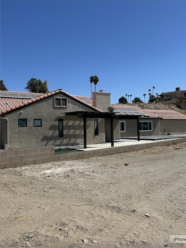 rear view of house featuring stucco siding, a tiled roof, and a chimney