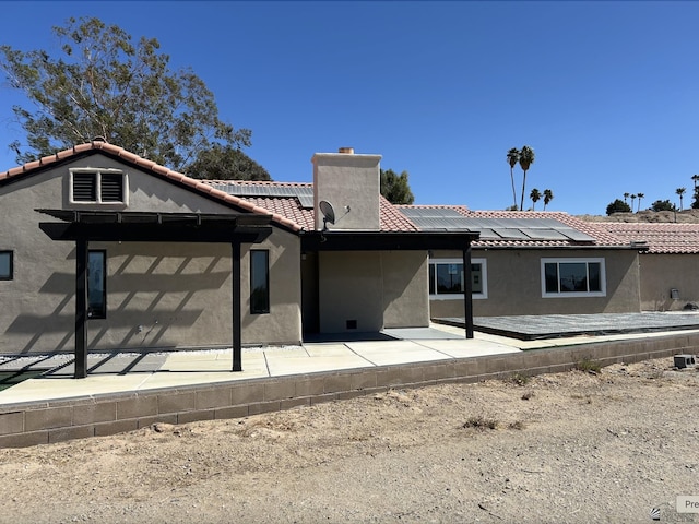 back of house with solar panels, a tile roof, stucco siding, a chimney, and a patio area