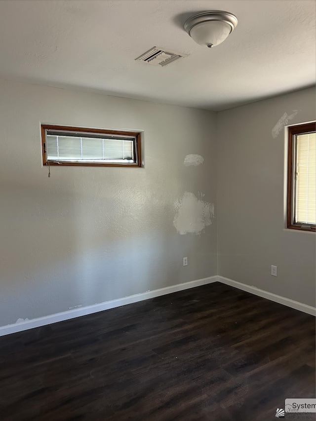 unfurnished room featuring visible vents, dark wood-type flooring, and baseboards