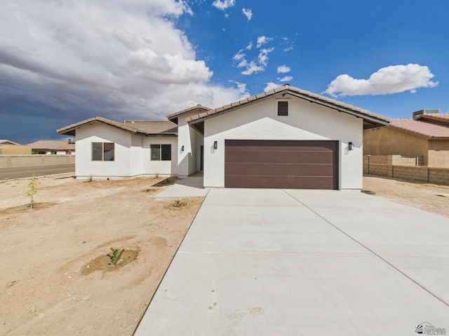 view of front of home with a garage, concrete driveway, fence, and stucco siding