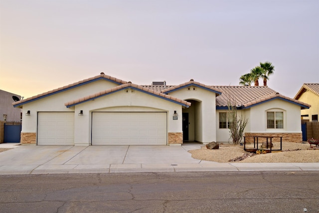 mediterranean / spanish-style home with driveway, stone siding, a tiled roof, an attached garage, and stucco siding