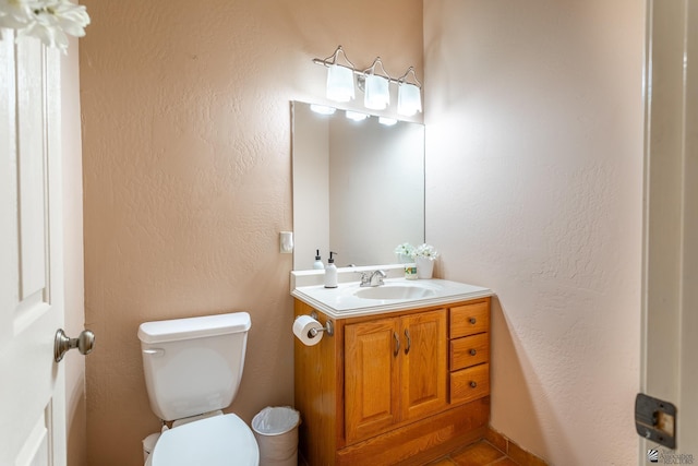 bathroom featuring toilet, a textured wall, and vanity