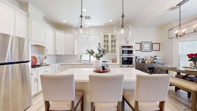 kitchen with appliances with stainless steel finishes, white cabinets, light countertops, and glass insert cabinets