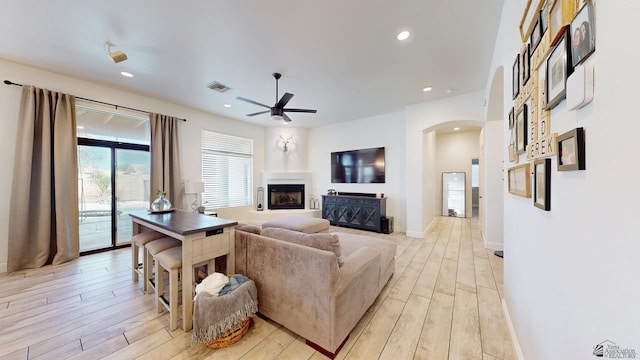 living area with light wood-style floors, arched walkways, a fireplace with raised hearth, and recessed lighting