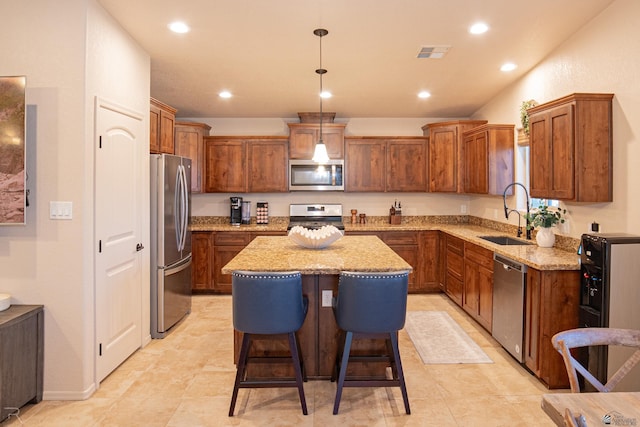 kitchen featuring visible vents, hanging light fixtures, a kitchen island, a sink, and appliances with stainless steel finishes