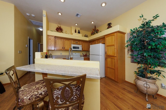 kitchen with light hardwood / wood-style flooring, kitchen peninsula, a towering ceiling, white appliances, and a breakfast bar