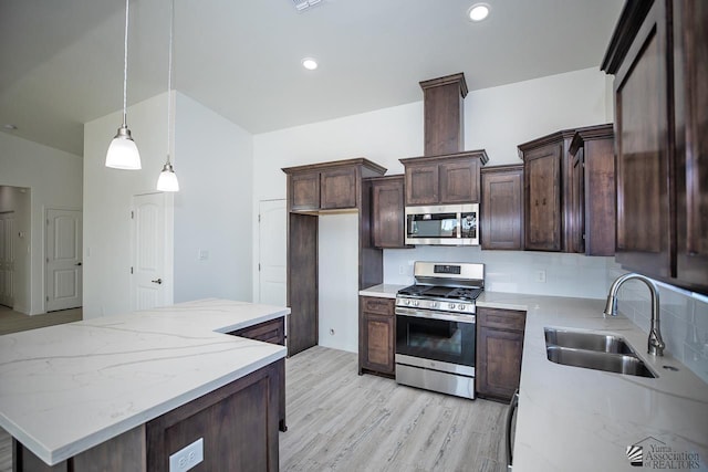 kitchen with stainless steel appliances, decorative light fixtures, light stone countertops, light hardwood / wood-style flooring, and sink