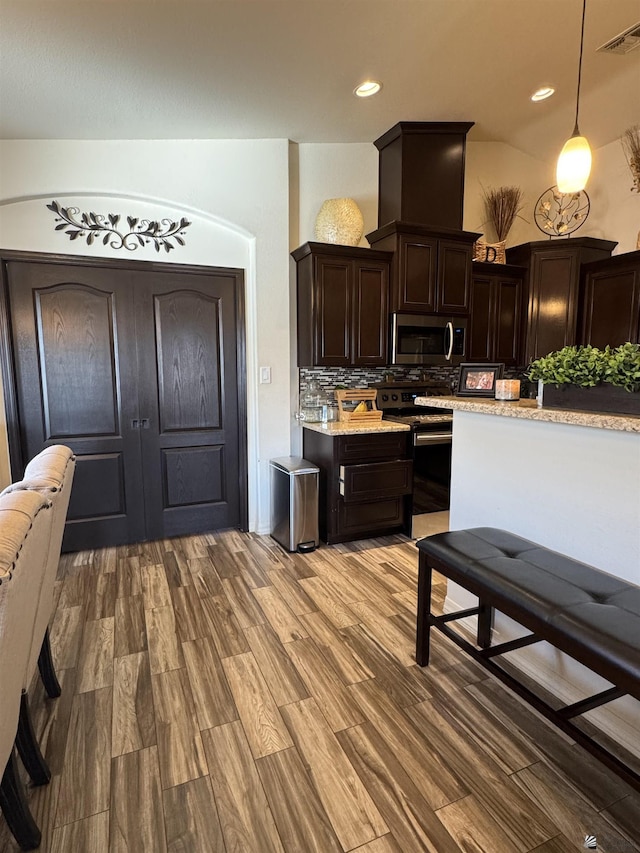 kitchen featuring appliances with stainless steel finishes, decorative light fixtures, decorative backsplash, dark brown cabinetry, and light wood-type flooring