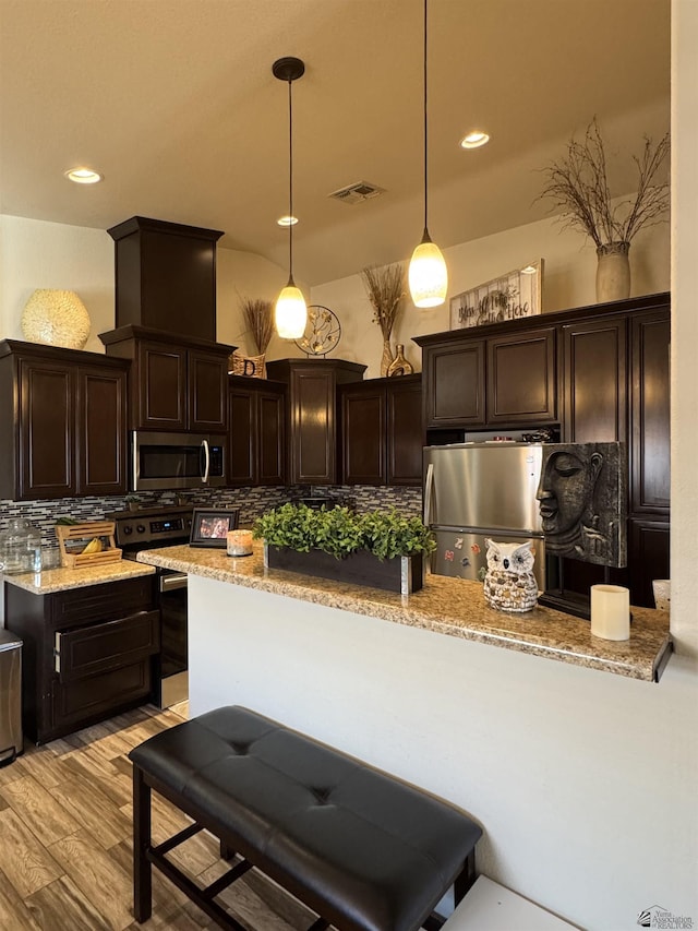 kitchen with hanging light fixtures, stainless steel appliances, dark brown cabinetry, light stone counters, and tasteful backsplash