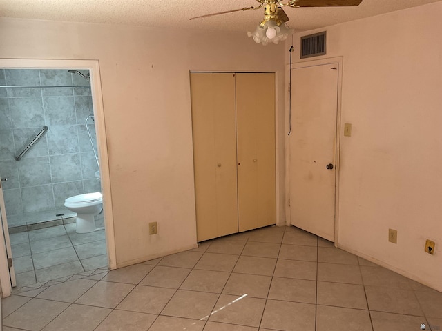 unfurnished bedroom featuring light tile patterned floors, tile walls, connected bathroom, a textured ceiling, and a closet