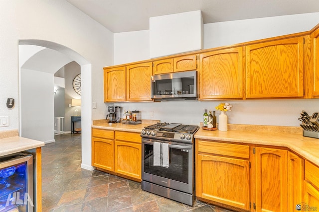kitchen featuring light countertops, arched walkways, stainless steel appliances, stone finish flooring, and wine cooler
