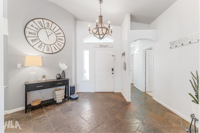 foyer entrance with baseboards, stone tile floors, arched walkways, and a notable chandelier