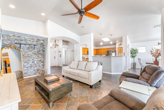 living area featuring arched walkways, stone tile floors, a ceiling fan, baseboards, and vaulted ceiling