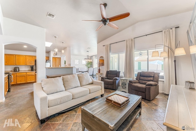 living room featuring visible vents, stone tile floors, ceiling fan with notable chandelier, and lofted ceiling