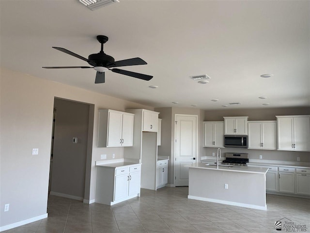 kitchen with appliances with stainless steel finishes, sink, light tile patterned floors, white cabinetry, and an island with sink